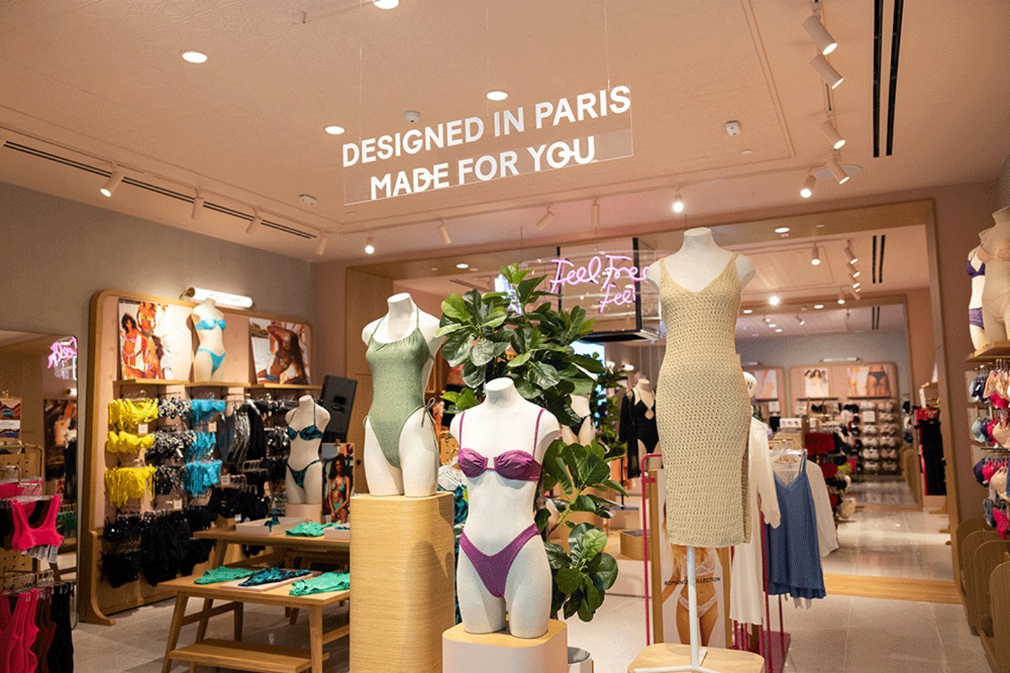 A clothing store interior displaying swimwear and dresses on mannequins, with the sign "Designed in Paris Made for You" above.